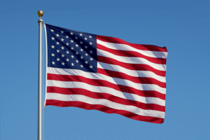 A clean photograph of the United States flag waving on a pole against a clear blue sky